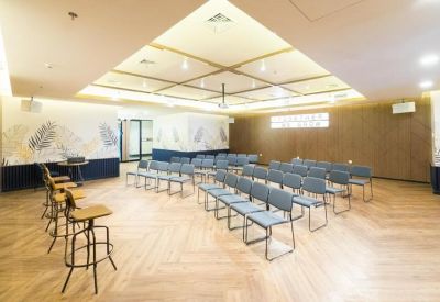 Bright multi-purpose event space with rows of grey chairs and warm wood-style flooring.