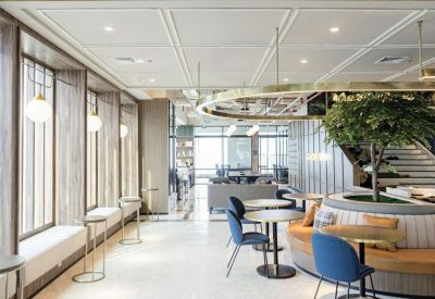 Sunlit cafe-style seating area with blue chairs, round tables, and an indoor tree.