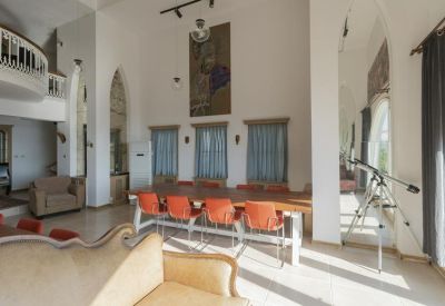 Communal area with a large table and orange chairs under high ceilings.