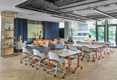 Spacious coworking area with several grey desks, ergonomic chairs, and industrial ceiling details.