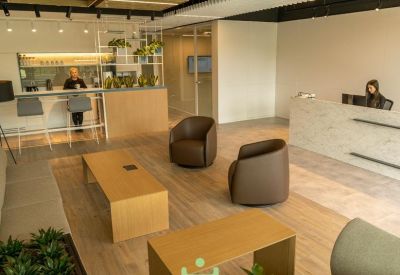 Spacious reception area with lounge seating, wooden coffee tables, and a front desk with a staff member.