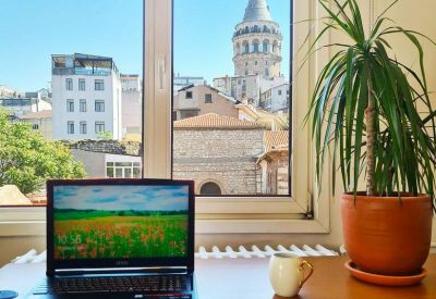 Bright workspace with a laptop on a wooden desk featuring a framed window view of Galata Tower.