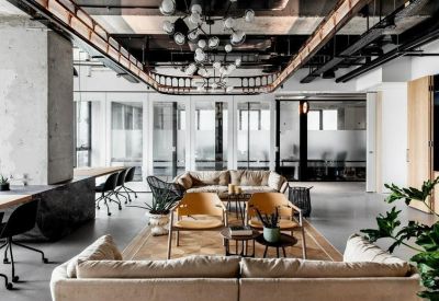 Spacious communal lounge with beige sofas, wooden chairs, and industrial ceiling details.