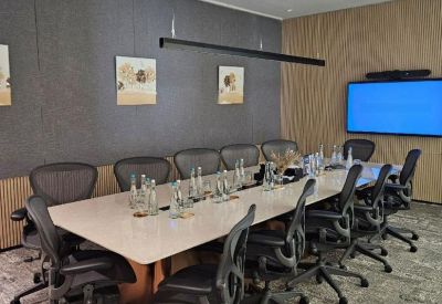 Professional boardroom featuring a long white table, ergonomic chairs, and wall-mounted screen.