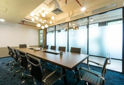 Professional meeting room with a long wooden table, ergonomic black chairs, and frosted glass walls.