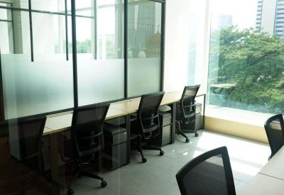 Workstations with ergonomic chairs positioned along a glass partition in a sunlit office environment.