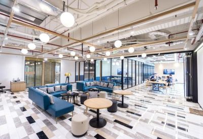 Bright open-plan workspace with blue sectional seating, round coffee tables, and glass-walled private offices.
