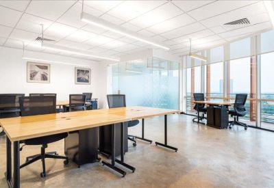 Spacious office area with light wood desks, floor-to-ceiling windows, and natural light.