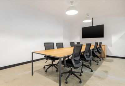 Modern conference room with a light wood table, black mesh chairs, and a wall-mounted screen.