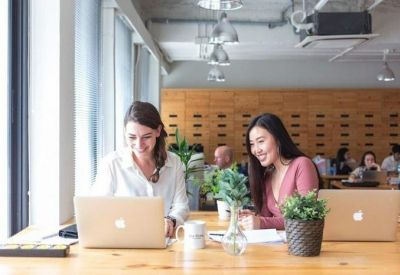 Spacious communal area with multiple people working on laptops at long wooden tables.