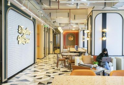Open-plan coworking space with various seating options, plants, and natural light from large windows.