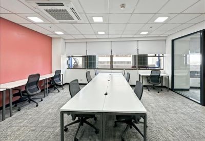 Open-plan coworking space with long white desks and a pink feature wall.