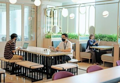 Coworking space with long communal tables, bench seating, and people working on laptops.