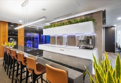Modern pantry area with a white marble island, breakfast bar seating, and lush green plants.