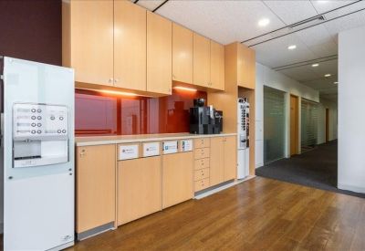 Communal kitchen area with light wood cabinetry, a coffee machine, and warm hardwood flooring.