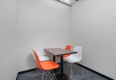 Small breakout area with a dark wood table and vibrant orange and white chairs.