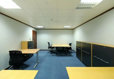 Four-person private office suite with wooden desks, black chairs, and blue carpet.