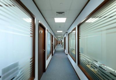 Long office corridor with wood-trimmed glass partitions and frosted privacy stripes.