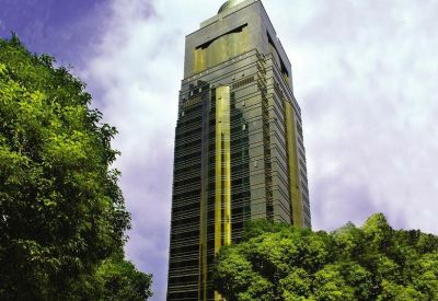 A dramatic low-angle view of the Apollo Building, 1440 Yan An Road tower set against a cloudy sky and green trees.
