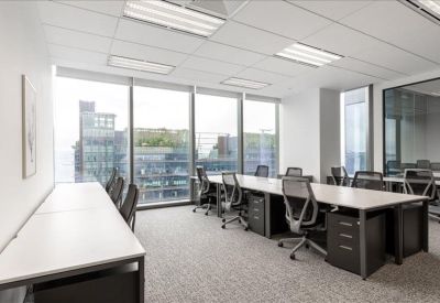 Bright open-plan office with long white desks and views of the city skyline through large windows.