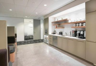 Modern office kitchen with light wood cabinetry and high-end coffee machines.