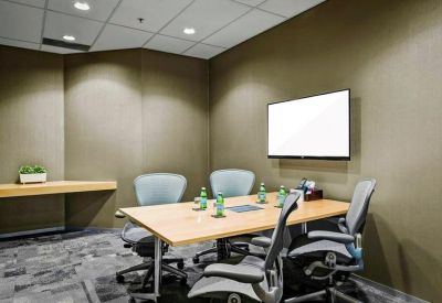 Small meeting room with four grey chairs, a wooden table, and a wall-mounted screen.