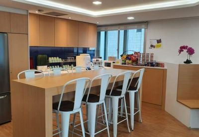 Modern office pantry featuring a high breakfast bar, white stools, and a large refrigerator.