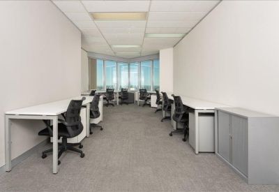 Long, open-plan workspace with multiple white desks, black ergonomic chairs, and large windows.