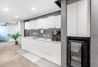 Modern office kitchen area with white cabinetry and a coffee machine.