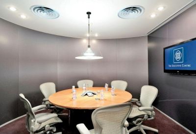 Circular meeting room with a round wooden table, ergonomic chairs, and grey wall panels.