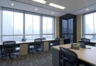 Bright open-plan office with multiple workstations and floor-to-ceiling windows showing city views.