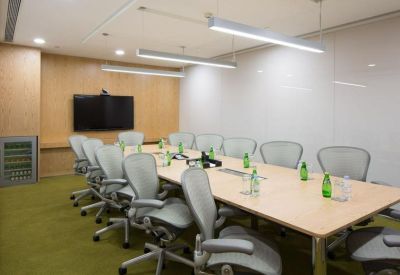 A professional boardroom featuring a long wooden table, grey mesh chairs, and green carpet.
