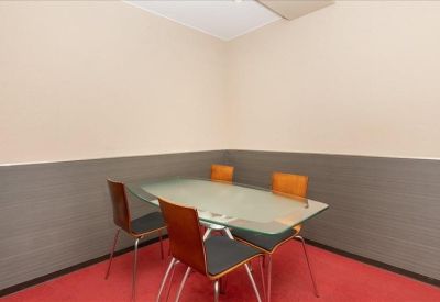 Small meeting room with a frosted glass table and four wooden chairs on a red carpet.