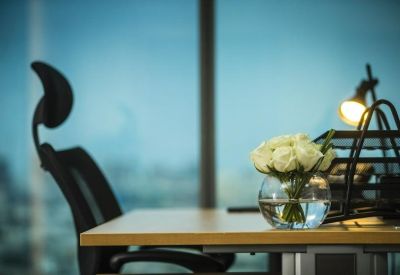 Desk detail featuring a glass vase with white roses and a modern desk lamp.
