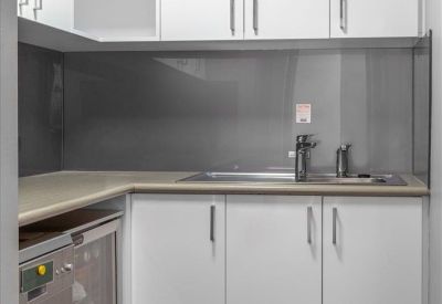 Sleek modern kitchenette with white cabinetry and dark grey backsplash.