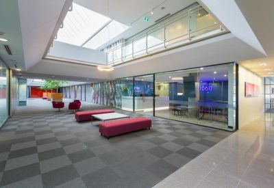 Bright open communal lounge with red benches and a view into glass-walled offices.