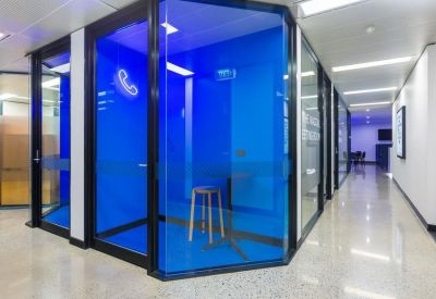 Private glass-walled phone booth with blue interior and wooden stool.
