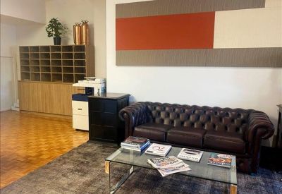 Waiting area with a dark leather tufted sofa, glass coffee table, and colorful wall art.