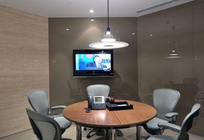 Small circular meeting room with a wooden table, grey chairs, and a wall-mounted television.