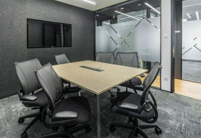 Modern meeting room with a light wood table, ergonomic black chairs, and a wall-mounted screen.