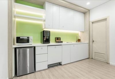 Modern office kitchen with white cabinetry, green backsplash, and integrated appliances.