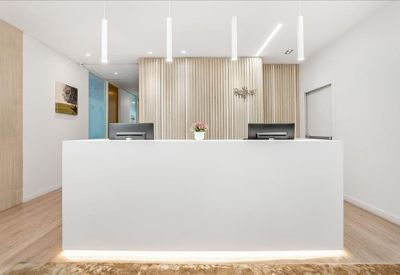 Sleek, minimalist white reception desk with light wood paneling and warm pendant lighting.