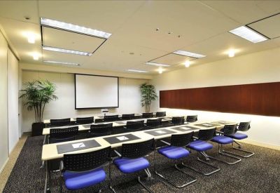 Classroom-style meeting room with a large projector screen and rows of blue chairs.