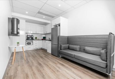Modern communal kitchen and breakout area with a large grey privacy sofa and wood-look flooring.