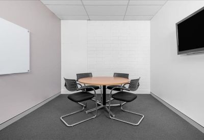 Small meeting room featuring a round timber table, four chairs, and a wall-mounted screen.