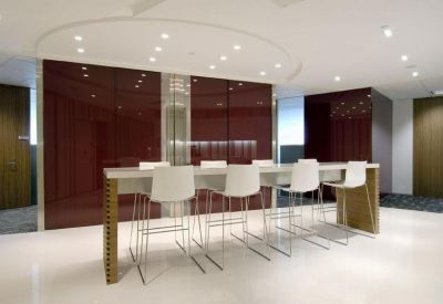 Modern communal breakout area featuring a long high-top table with white stools and a red feature wall.