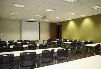 Spacious seminar room with rows of desks, black chairs, and a large projection screen.
