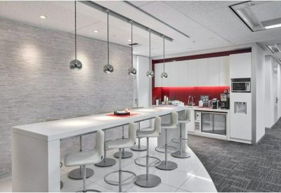 Modern communal kitchen area with a long white breakfast bar and red backsplash.