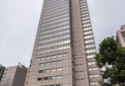 External view of the towering stone-facade Shinjuku Park Tower against an overcast sky.