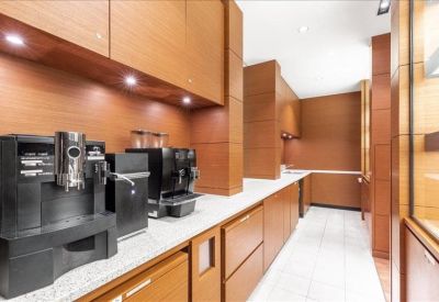 Sleek office kitchenette with dark coffee machines and warm wood cabinetry.